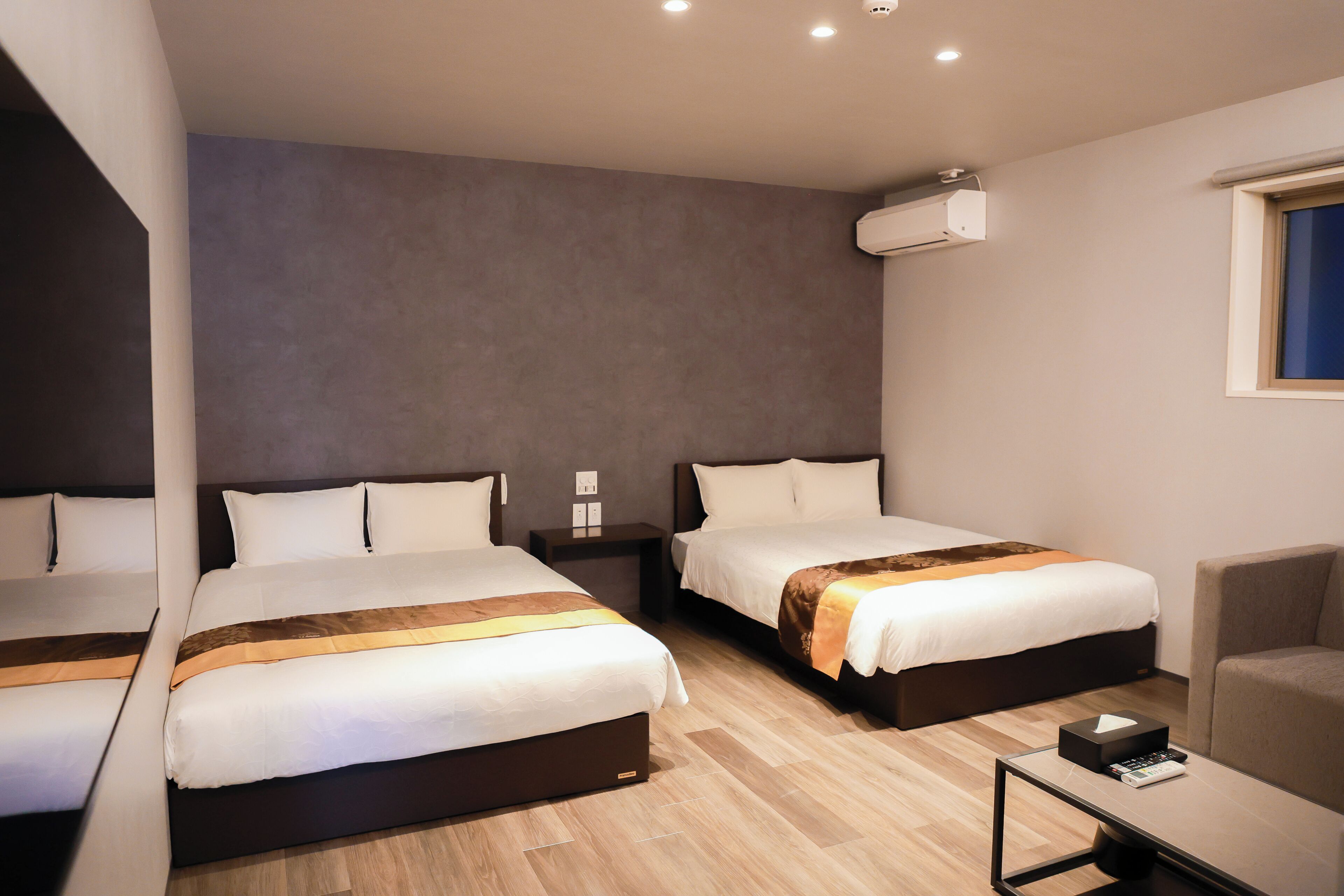 A hotel room with two beds, a small table, a chair, and a window.