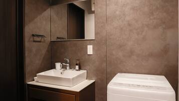 Un baño con un lavabo blanco, un espejo, un perchero para toallas y una lavadora blanca.