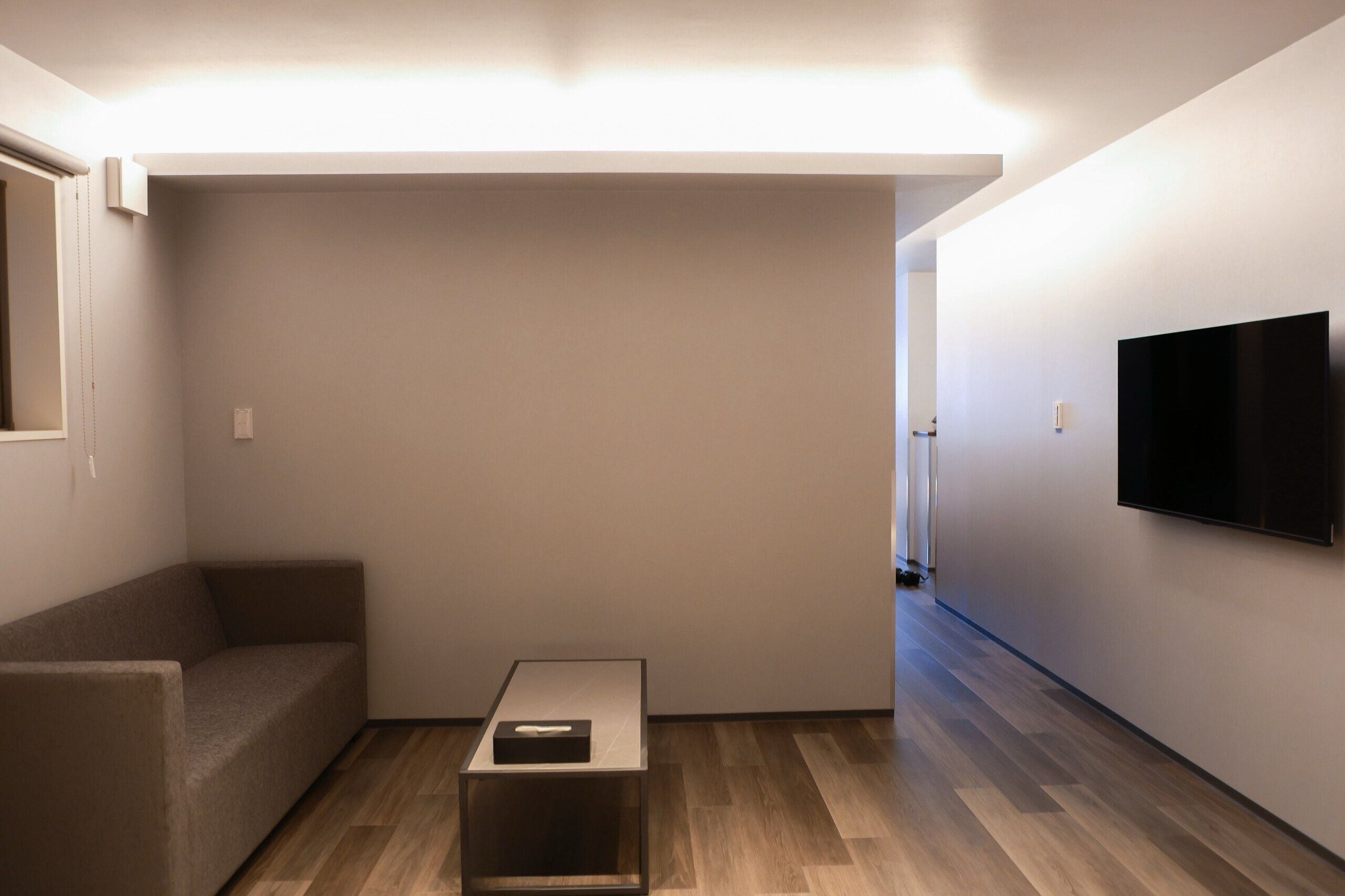 A minimalist living room with a sofa, a coffee table, and a flat-screen TV mounted on the wall.