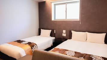 A hotel room with two beds, a window with blinds, a bedside table with a lamp, and a wall-mounted phone.