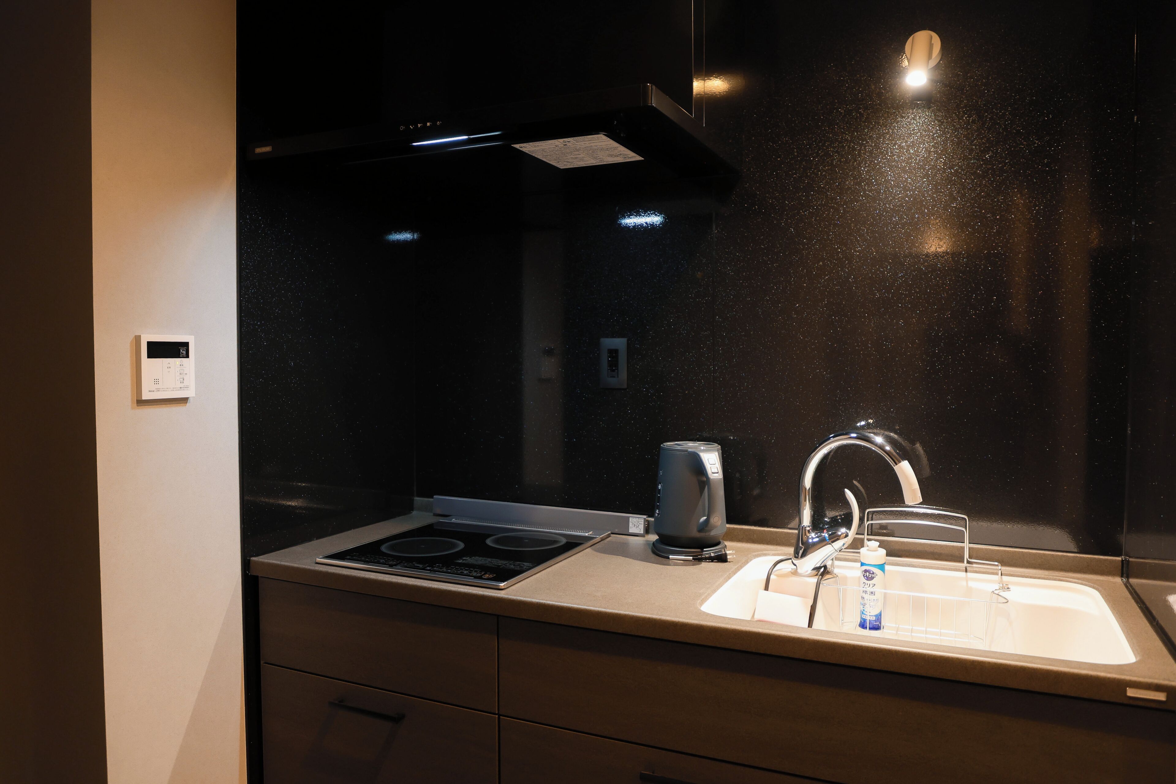 A modern kitchen with a stainless steel sink, a kettle, and a stove.