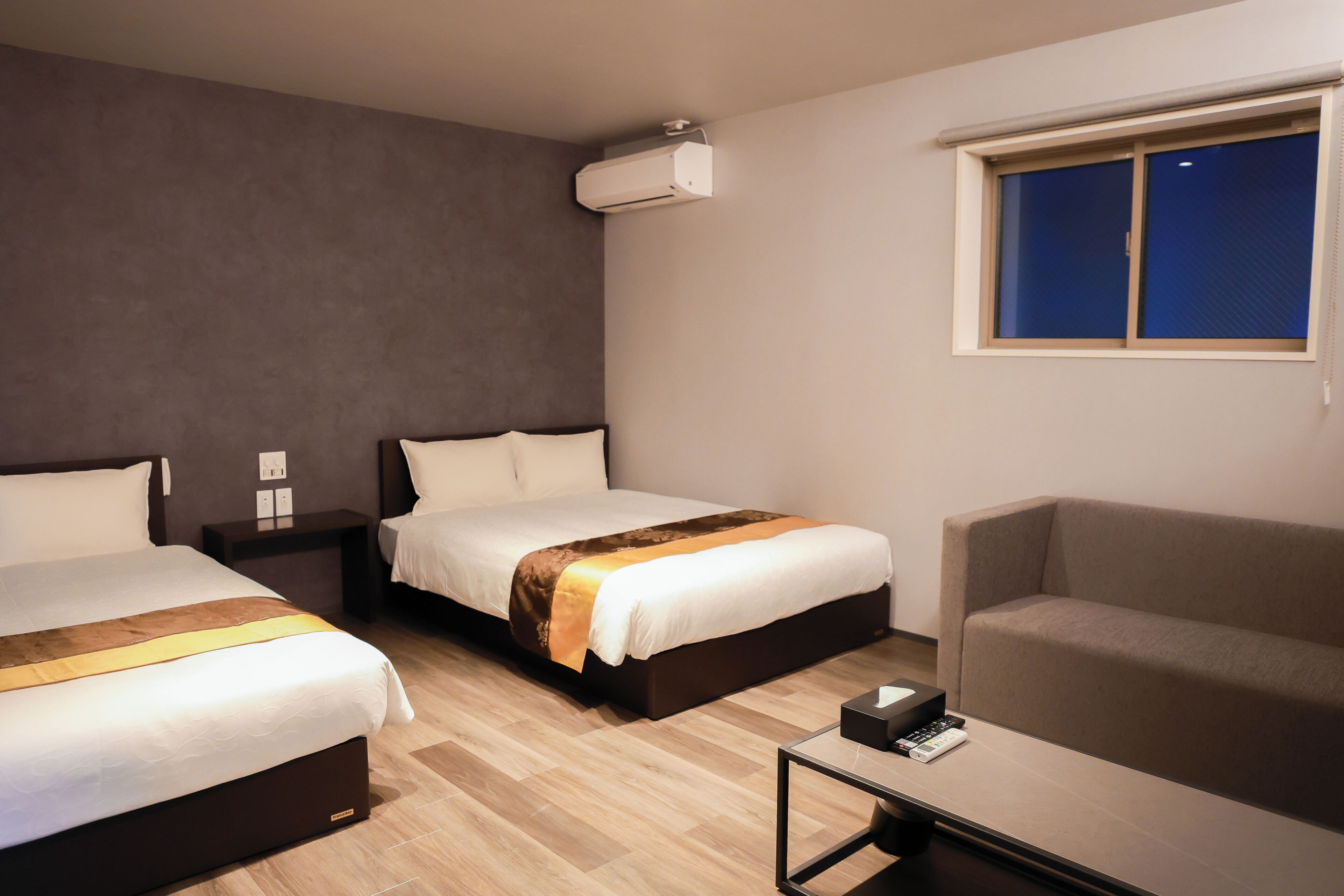 Ett hotellrum med två sängar, en soffa, ett litet bord och ett fönster.