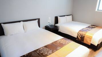 A hotel room with two beds, each with a white bedspread and a brown decorative runner. There is a nightstand with a lamp between the beds.