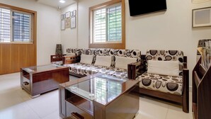 Una sala de estar con un sofá, una mesa de centro, un televisor montado en la pared y una ventana con persianas.