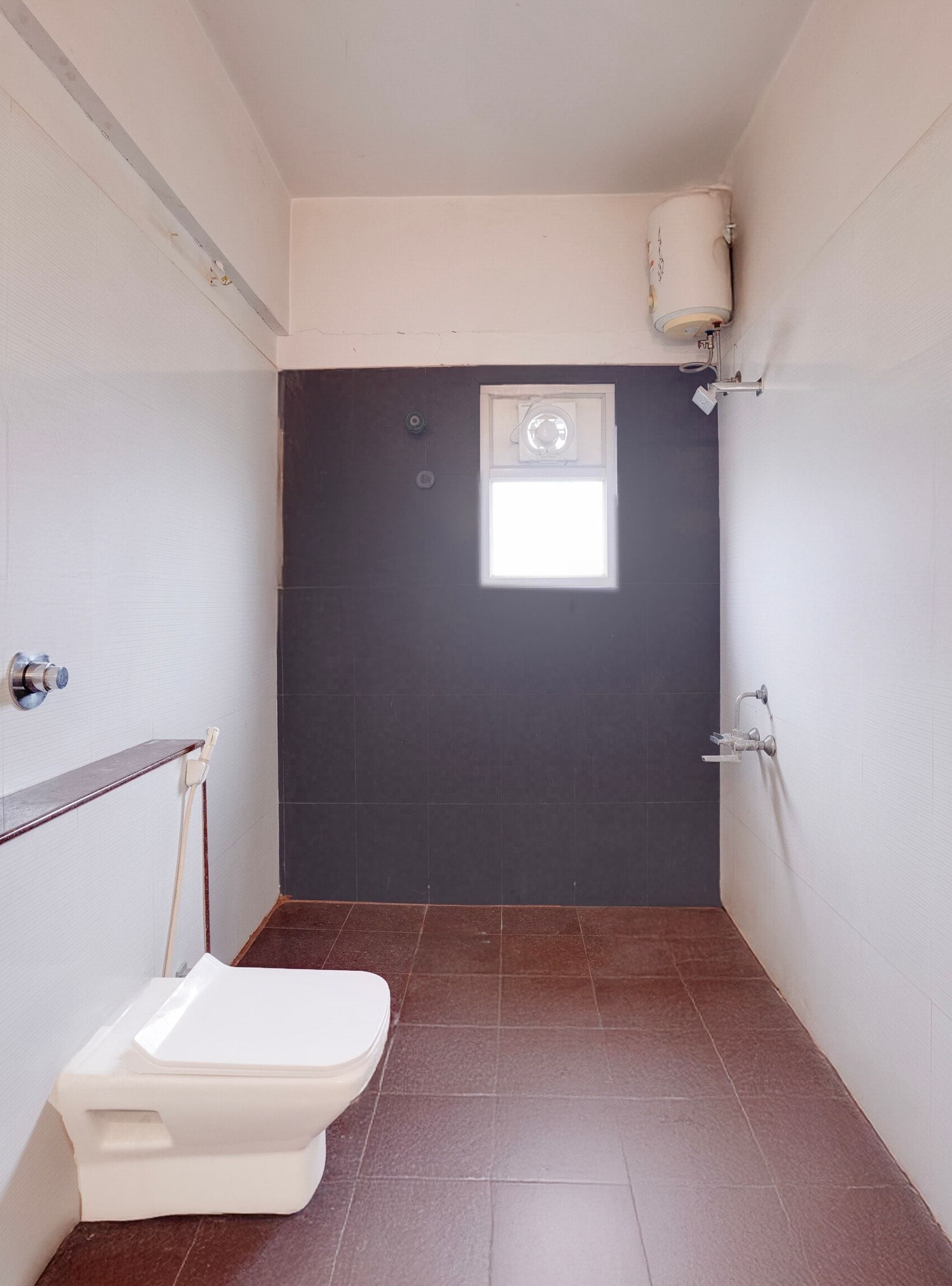 Une petite salle de bain étroite, avec des toilettes, une fenêtre et un chauffe-eau fixé au mur.