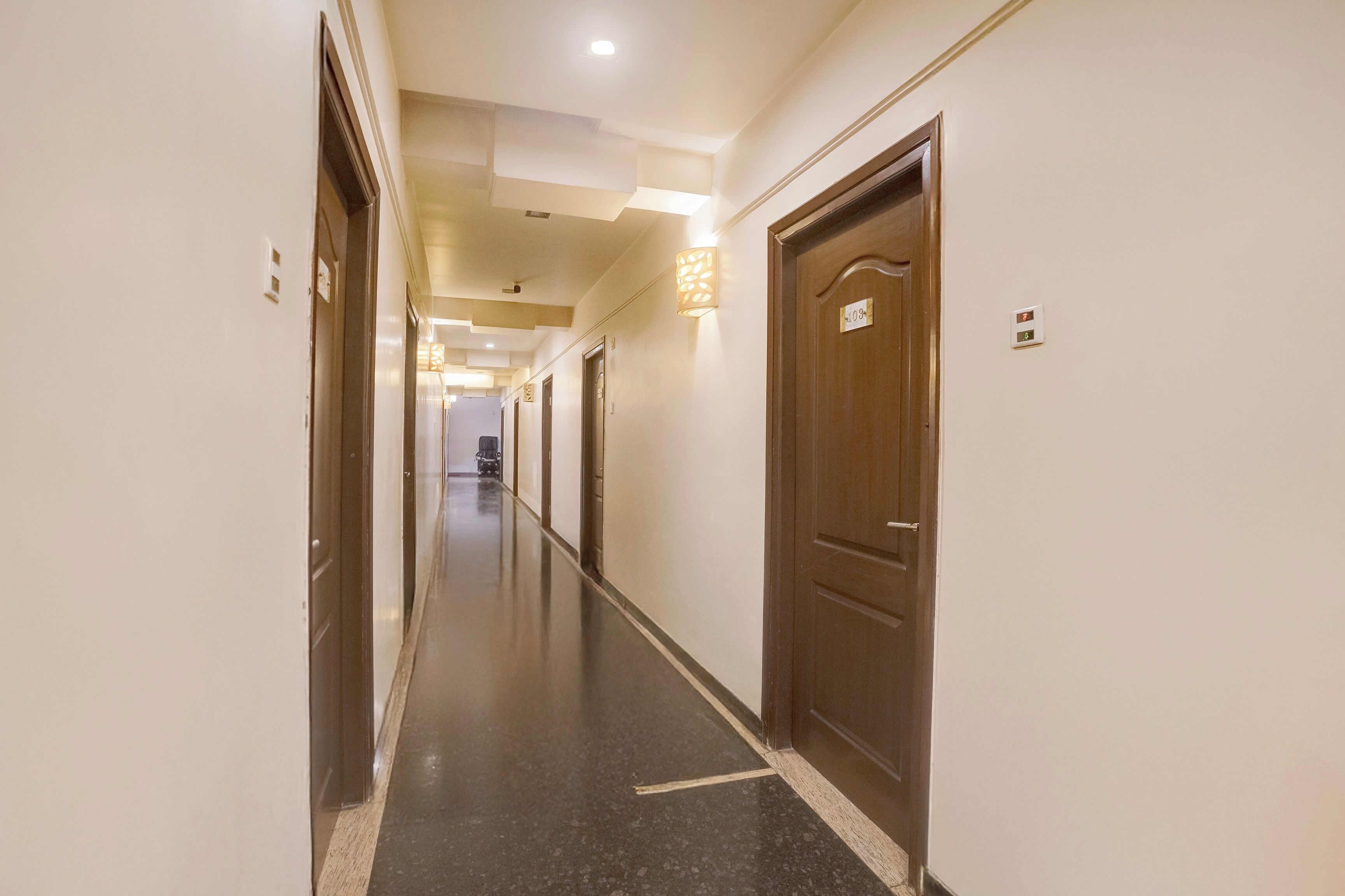 A hotel corridor with doors on both sides, a light fixture on the left, and a door with a number plate on the right.