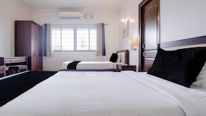 Habitación de hotel con dos camas, un escritorio, una silla, unidad de aire acondicionado, ventana con cortinas y una lámpara de pared.