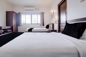 Habitación de hotel con dos camas, un escritorio, una silla, unidad de aire acondicionado, ventana con cortinas y una lámpara de pared.