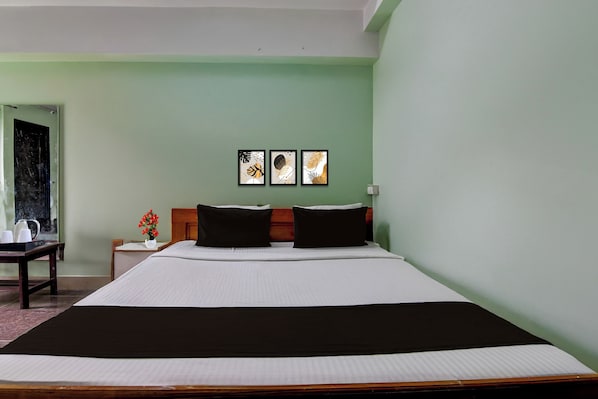 A hotel room with a large bed, two black pillows, a nightstand with a vase of flowers, and two framed artworks on the wall. - Super Collection O Jalpaiguri Formerly (Jalpaiguri)