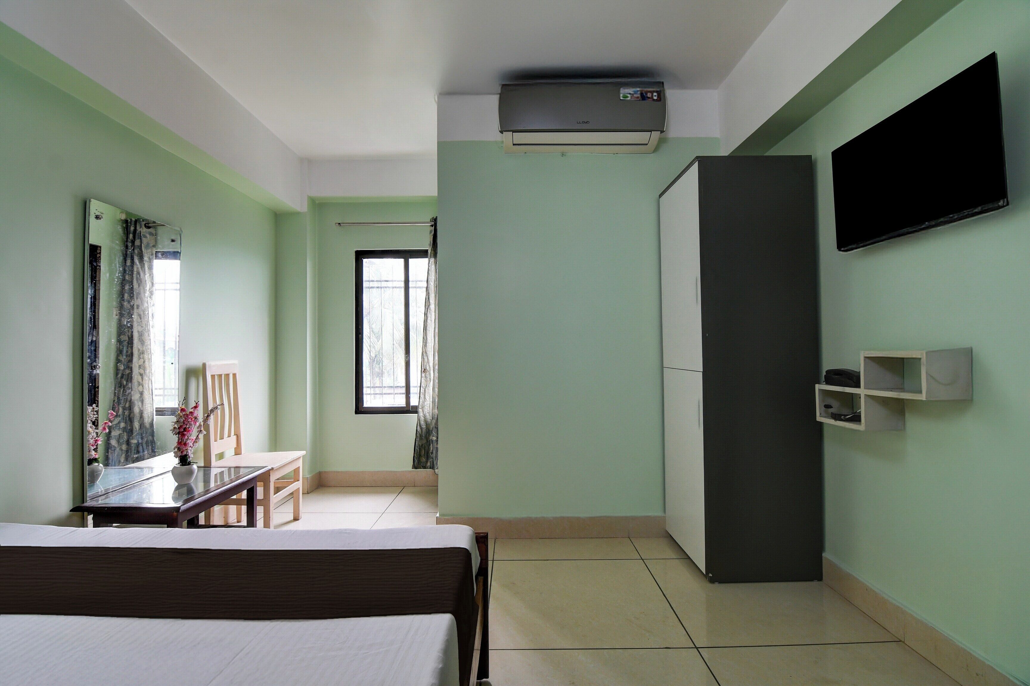 Habitación de hotel con cama, escritorio, silla, armario, televisor de pantalla plana y ventana con cortinas.