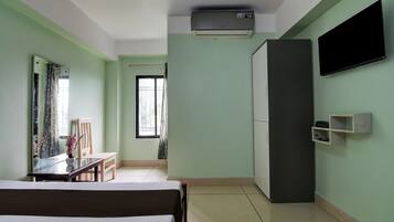 Habitación de hotel con cama, escritorio, silla, armario, televisor de pantalla plana y ventana con cortinas.