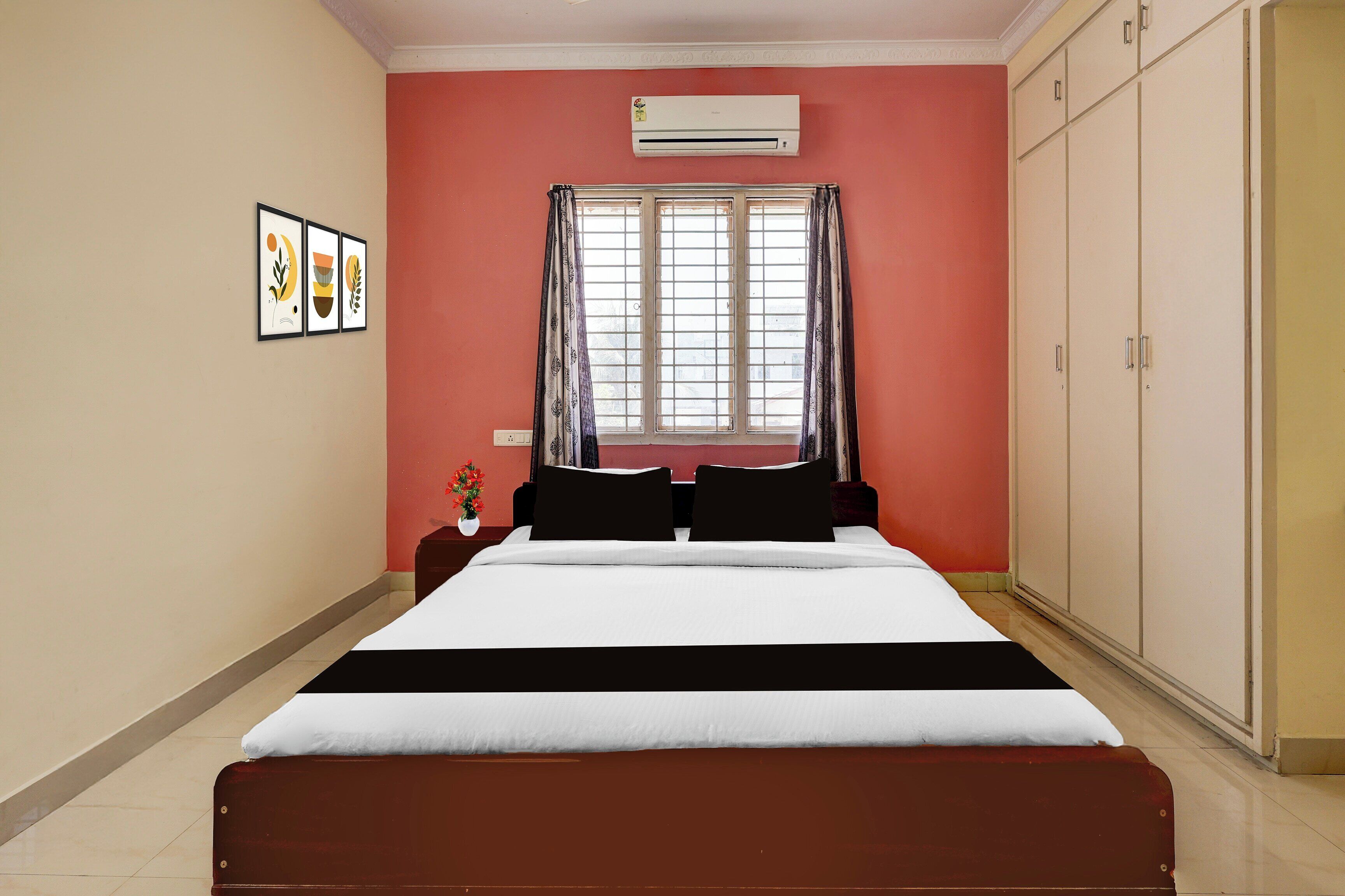 A bedroom with a bed, a window with curtains, an air conditioner, and a wardrobe.