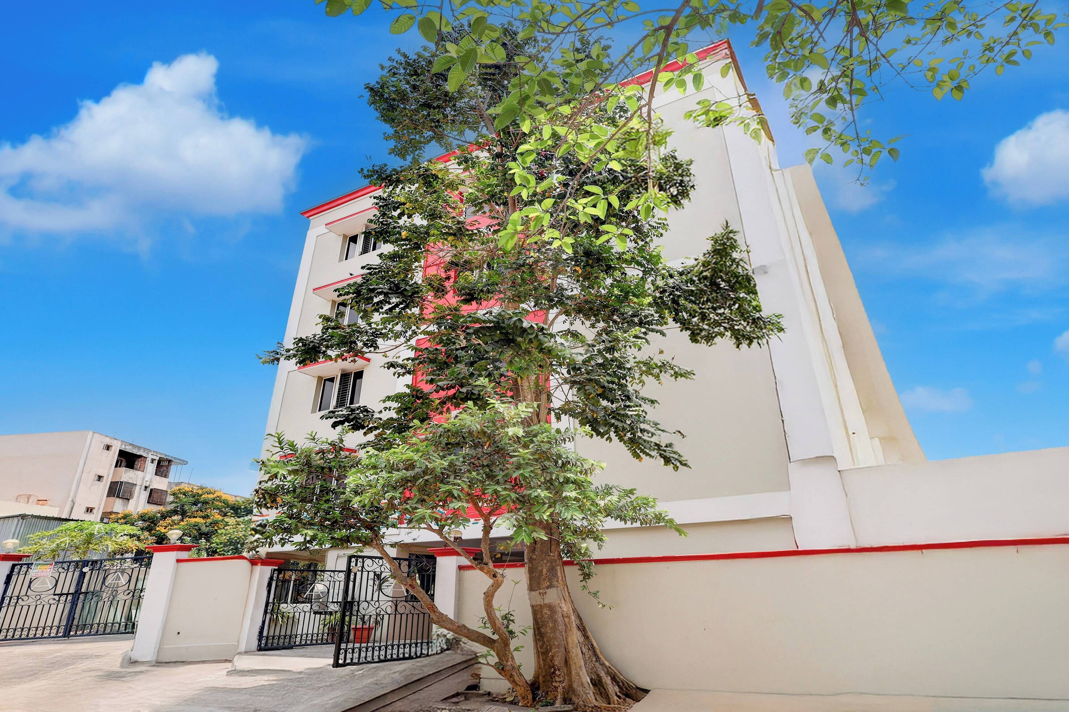 A multi-story building with a white facade and red trim, surrounded by greenery and a gated entrance.