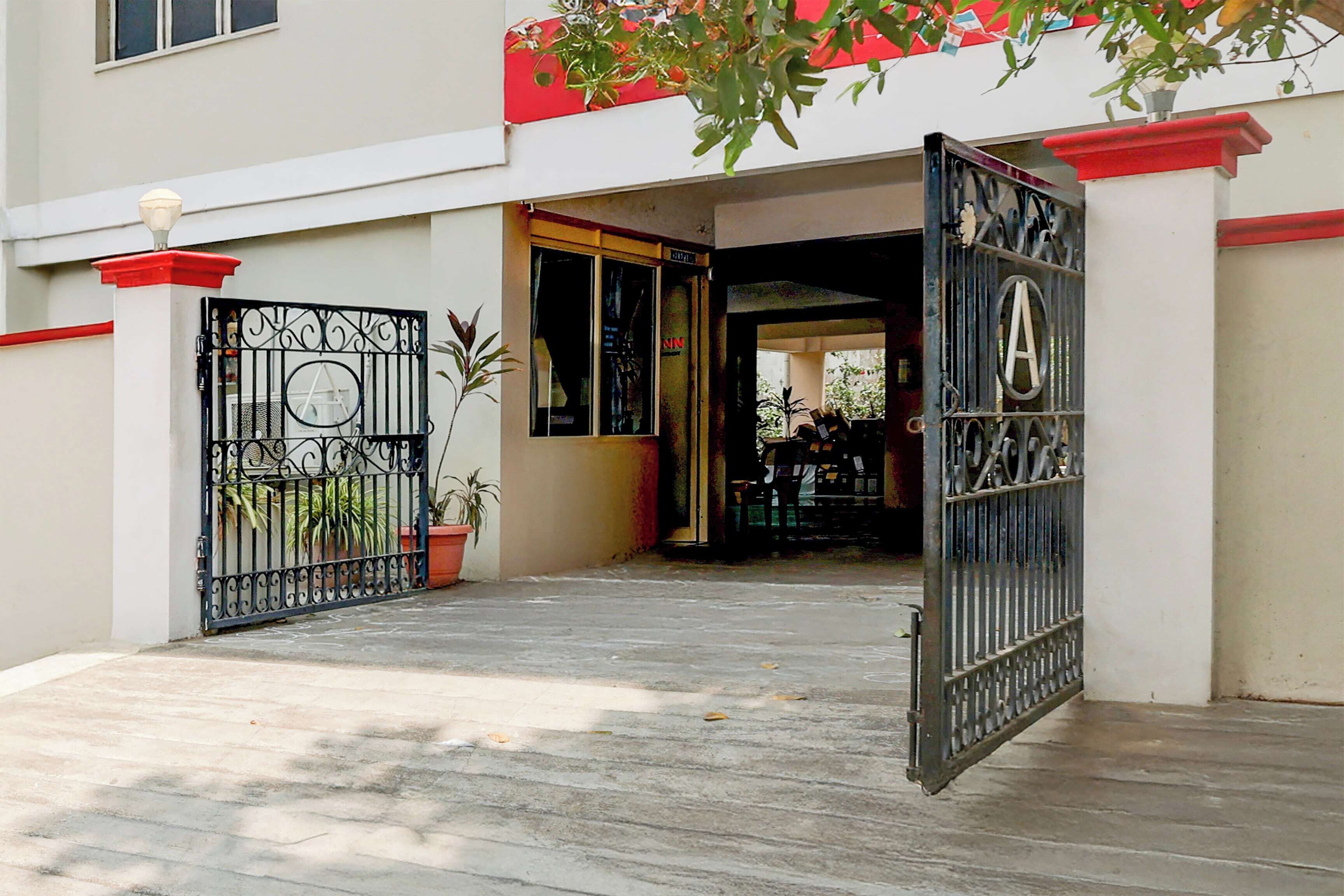 Entrada fechada por portão para um edifício com telhado vermelho, um vaso de planta e um portão de metal com o emblema 'A'.