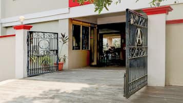 Entrada fechada por portão para um edifício com telhado vermelho, um vaso de planta e um portão de metal com o emblema 'A'.