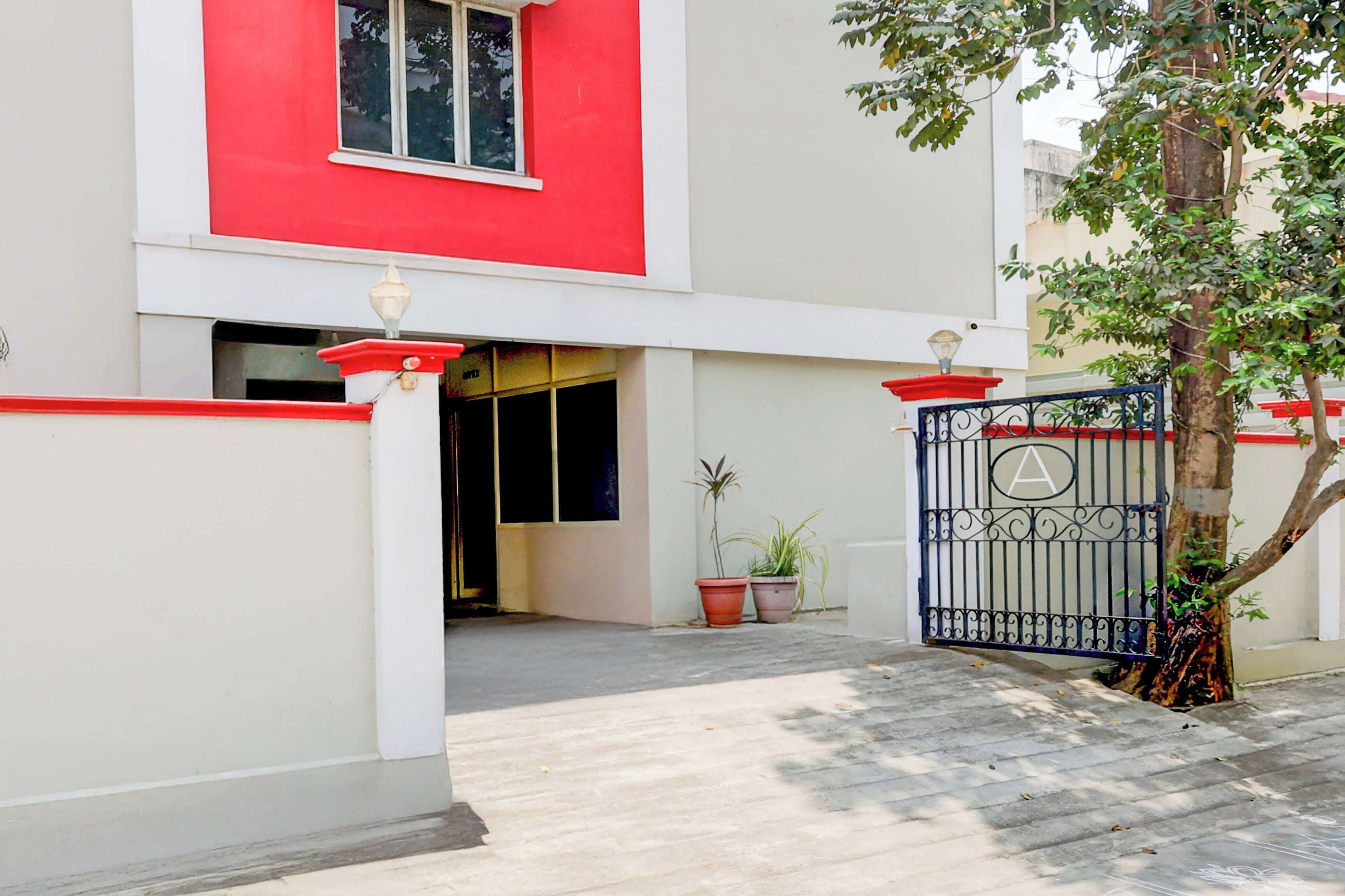 Uma entrada fechada por portão para um edifício com fachada em vermelho e branco, um vaso de planta e uma árvore.