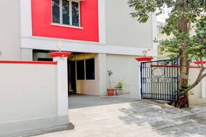 Una entrada con reja a un edificio de fachada roja y blanca, una planta en maceta y un árbol.