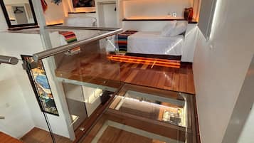 Une pièce de taille réduite comprenant un lit, une cloison en verre et un petit coin cuisine.