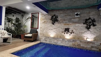 Une piscine bordée d’un muret en pierre, avec une chaise et des plantes en pot.