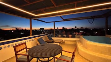 Un espace extérieur aménagé avec une table et des chaises, un jacuzzi et une vue sur le paysage urbain au crépuscule.