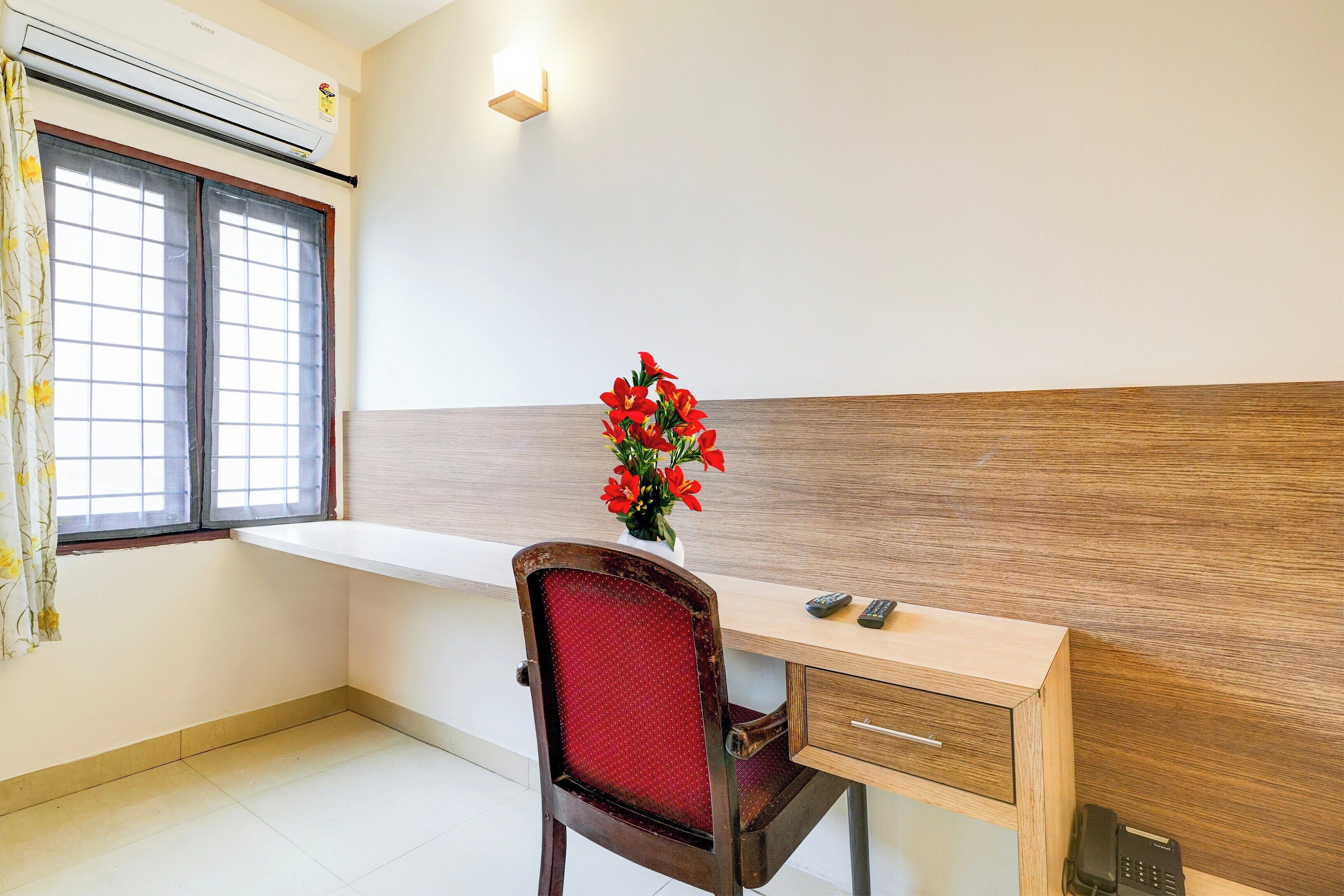 A room with a desk, chair, window, and a wall-mounted light fixture.