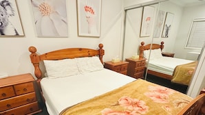 Un dormitorio ordenado con una cama de madera, una mesita de noche, un aparador y un espejo grande.