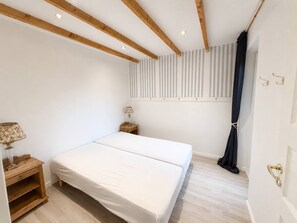 A bedroom with a bed, a nightstand, a lamp, a window with blinds, and a door with a handle. - Panoramic sea view direct sandy beach Skagen South (Ålbæk)