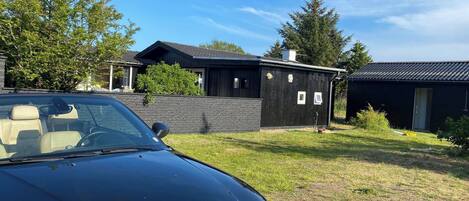 A black car parked in front of a house with a brick wall and a wooden structure.