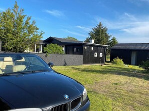 Ein schwarzes Auto vor einem Haus mit Backsteinmauer und Holzkonstruktion.