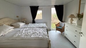 Quarto com cama grande, penteadeira, cadeira e janela com cortinas.