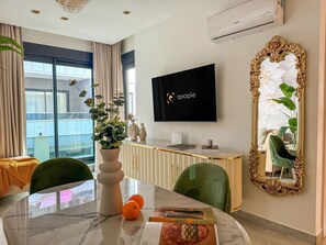 Ein modernes Hotelzimmer mit einem Marmortisch, grünen Polsterstühlen, einem großen Spiegel mit aufwendigem Rahmen und einem flachbildfernseher an der Wand.