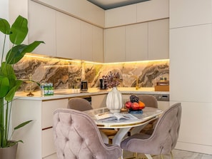 A modern kitchen with a marble backsplash, a dining area with a glass table, and two upholstered chairs. - Qoople Legend 36 В-01 100 Meter vom Strand entfernt by Interhome (Alanya)
