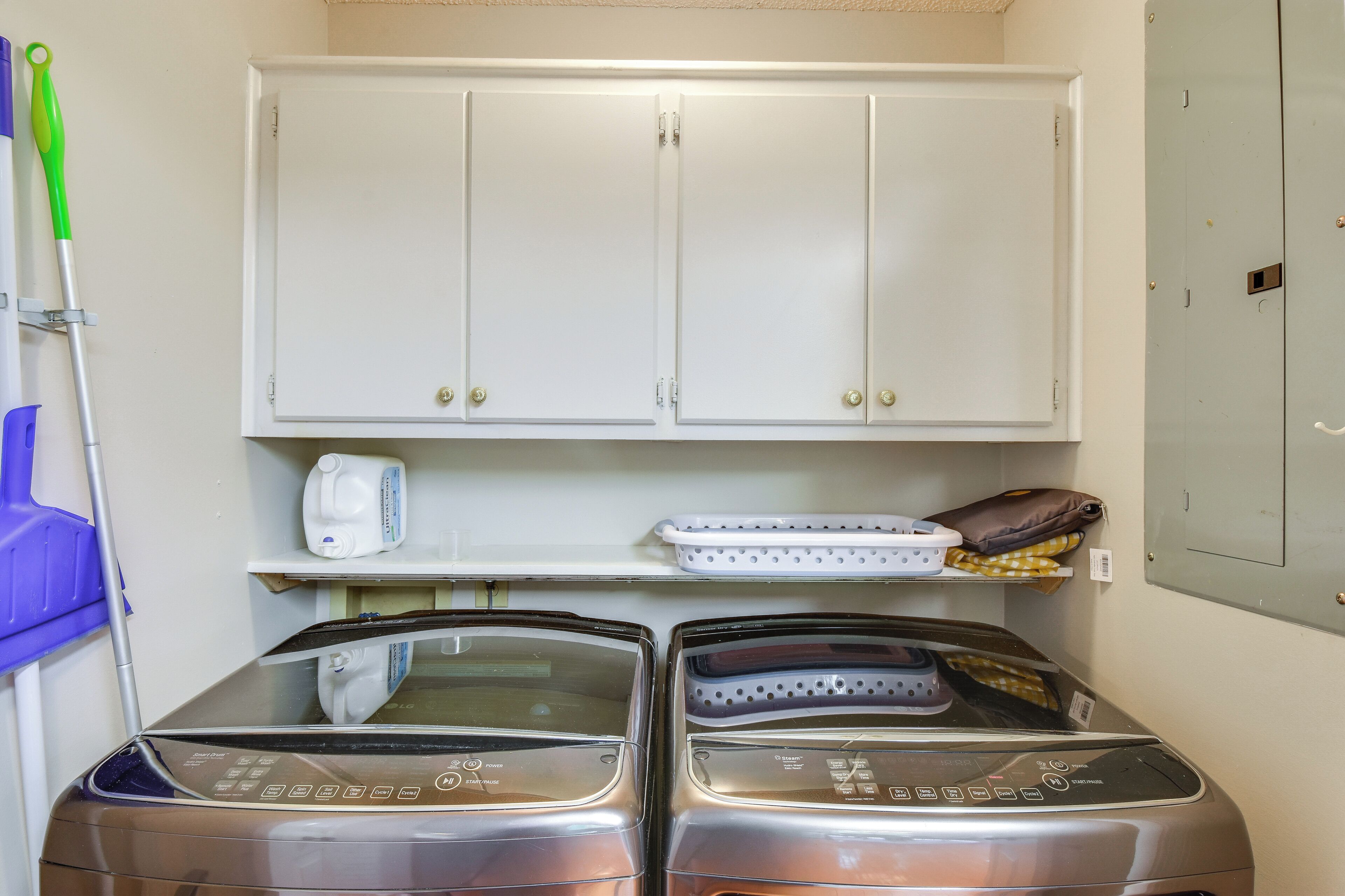 A laundry room with two washing machines, a cabinet, and a shelf with a bottle and a bag.