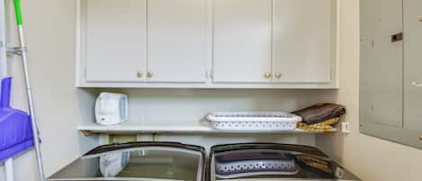 A laundry room with two washing machines, a cabinet, and a shelf with a bottle and a bag.