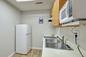 Eine kleine Küche mit integriertem Mikrowellenherd, einer Edelstahl-Spüle und einem kleinen Kühlschrank.