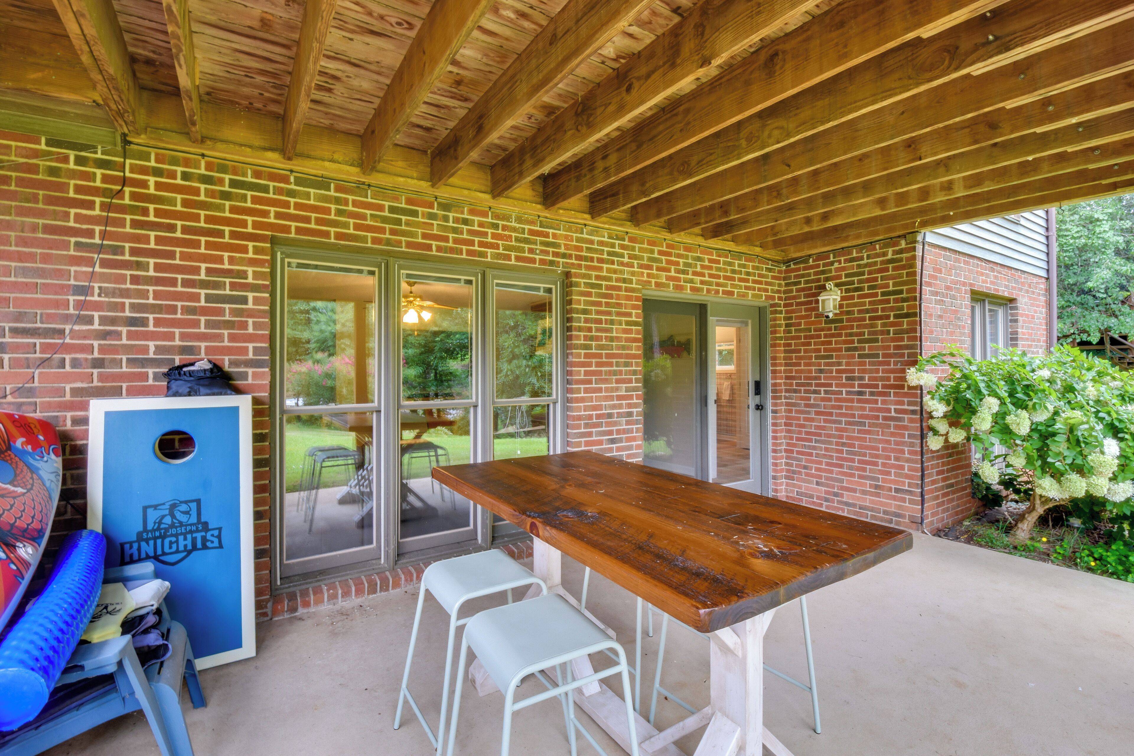 An outdoor patio with a wooden table and two white metal stools, a blue vending machine, and a brick wall.