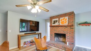 A living room with a fireplace, a ceiling fan, and a television mounted on the wall. - Clemson Basecamp! Lake Keowee Hideaway (Seneca)