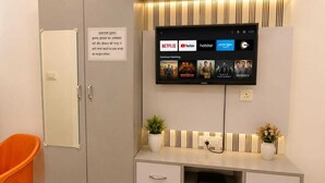A room with a television mounted on the wall displaying various streaming services. There is a cabinet with drawers and a sign on the door. - KU Residency (Varanasi)