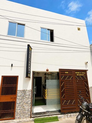 Un edificio con un cartel que indica habitaciones con aire acondicionado y sin aire acondicionado, una motocicleta estacionada adelante y una entrada con portón.