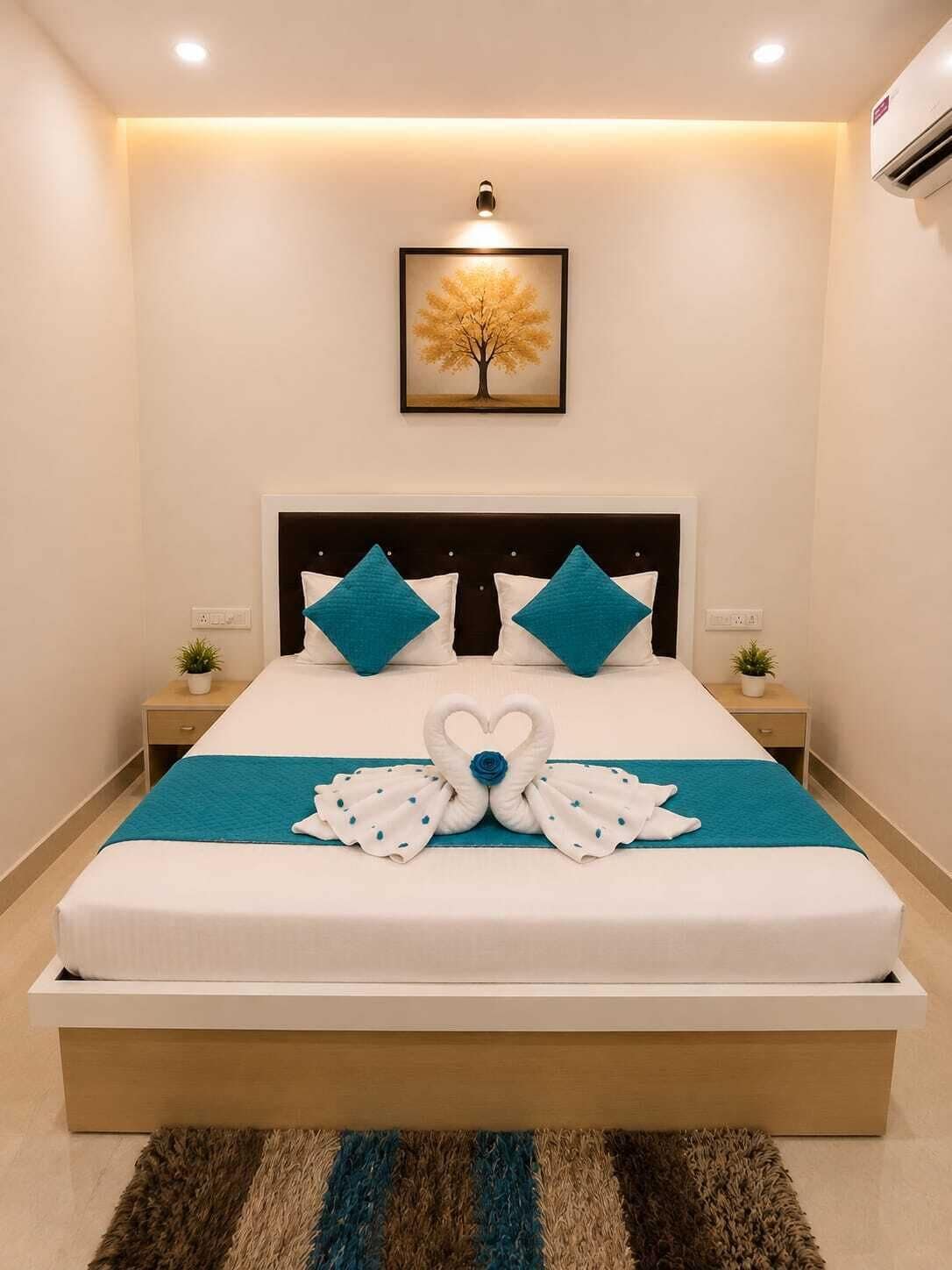 A neatly made bed with a teal bedspread, two pillows, and a heart-shaped towel arrangement.