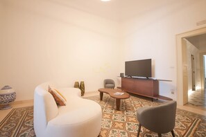 A modern living room with a sofa, armchair, coffee table, and a flat-screen TV on a wooden cabinet. - TD Palazzo Fiume 1 Heart of Polignano (Polignano a Mare)