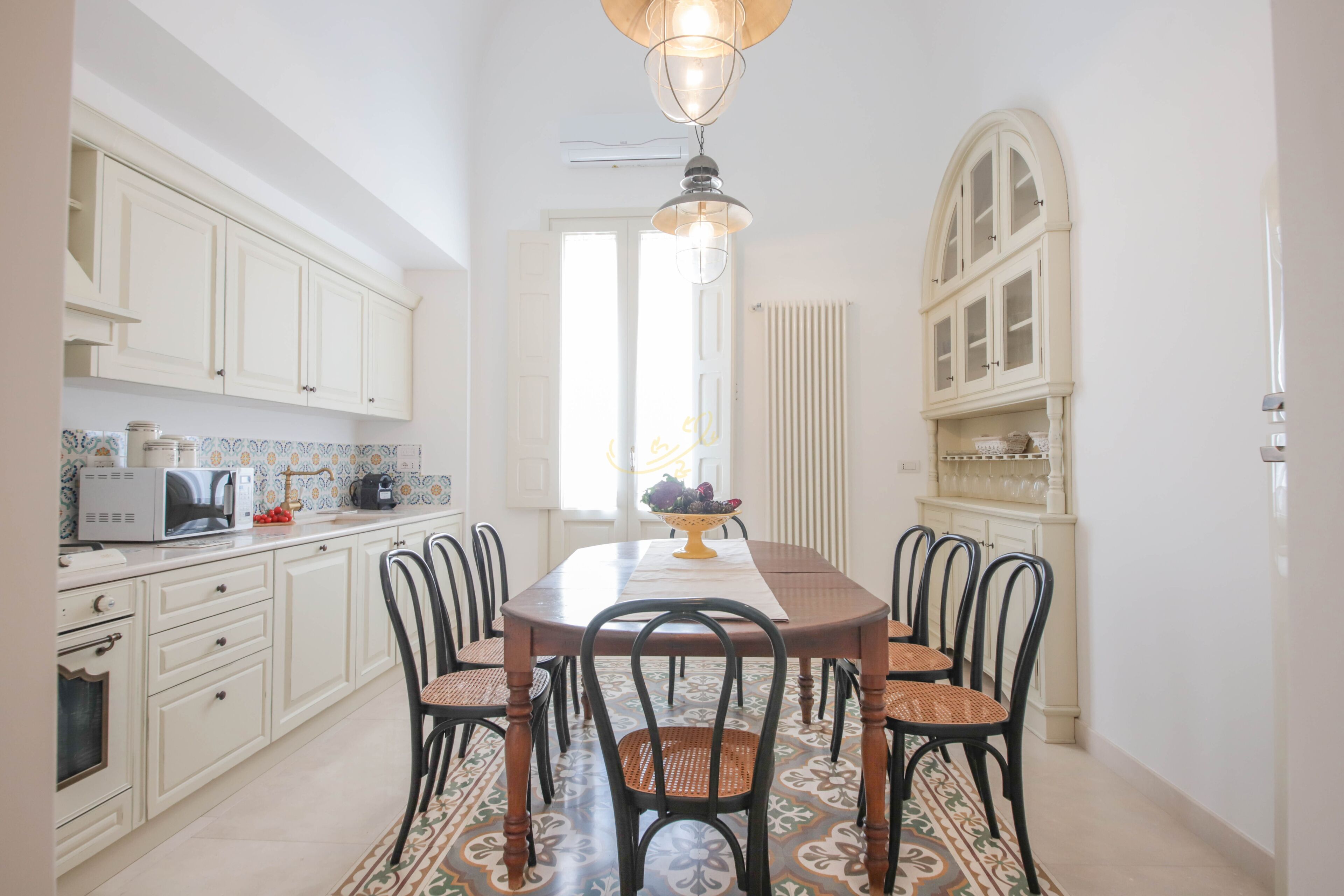 Uma sala de jantar com uma mesa redonda, seis cadeiras e um candelabro.