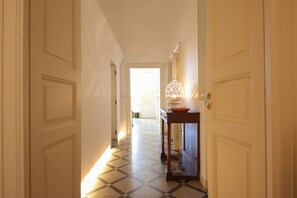 Un couloir doté d’un revêtement de sol à motifs, une table surmontée d’une lampe décorative et une porte donnant sur une autre pièce.