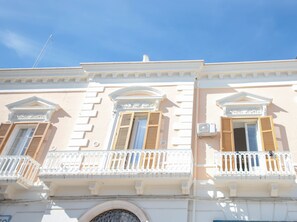 Une façade d’immeuble présentant des éléments architecturaux classiques, notamment des colonnes, des pilastres et un balcon agrémenté de balustrades décoratives.