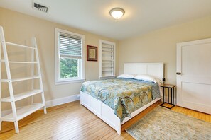 Ein Schlafzimmer mit einem Bett, einer weißen Leiter, einem Fenster mit Jalousien, einer Tür und einem kleinen Tisch.