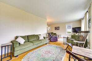 Ein Wohnzimmer mit einem grünen Sofa, einem Liegesessel, einem Holztisch und einem gemusterten Teppich.