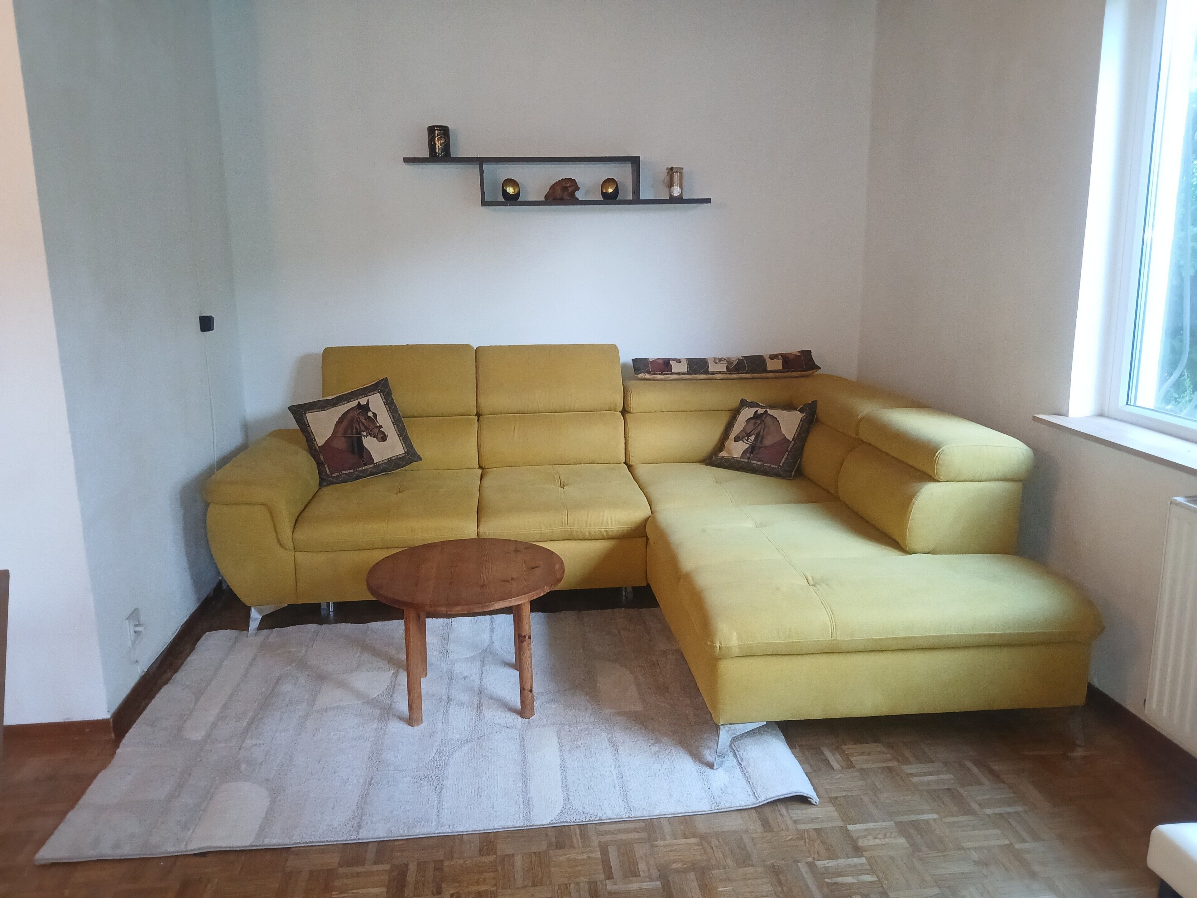 Un sofà seccional groc amb dos coixins decoratius, una taula de fusta petita i una catifes blanca.