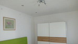 A bedroom with a green headboard, a white bed, a wooden and white wardrobe, and a single light fixture on the ceiling. - Apartment 'Weidenblick' with Mountain View, Private Terrace and Wi-Fi (Schottwien)