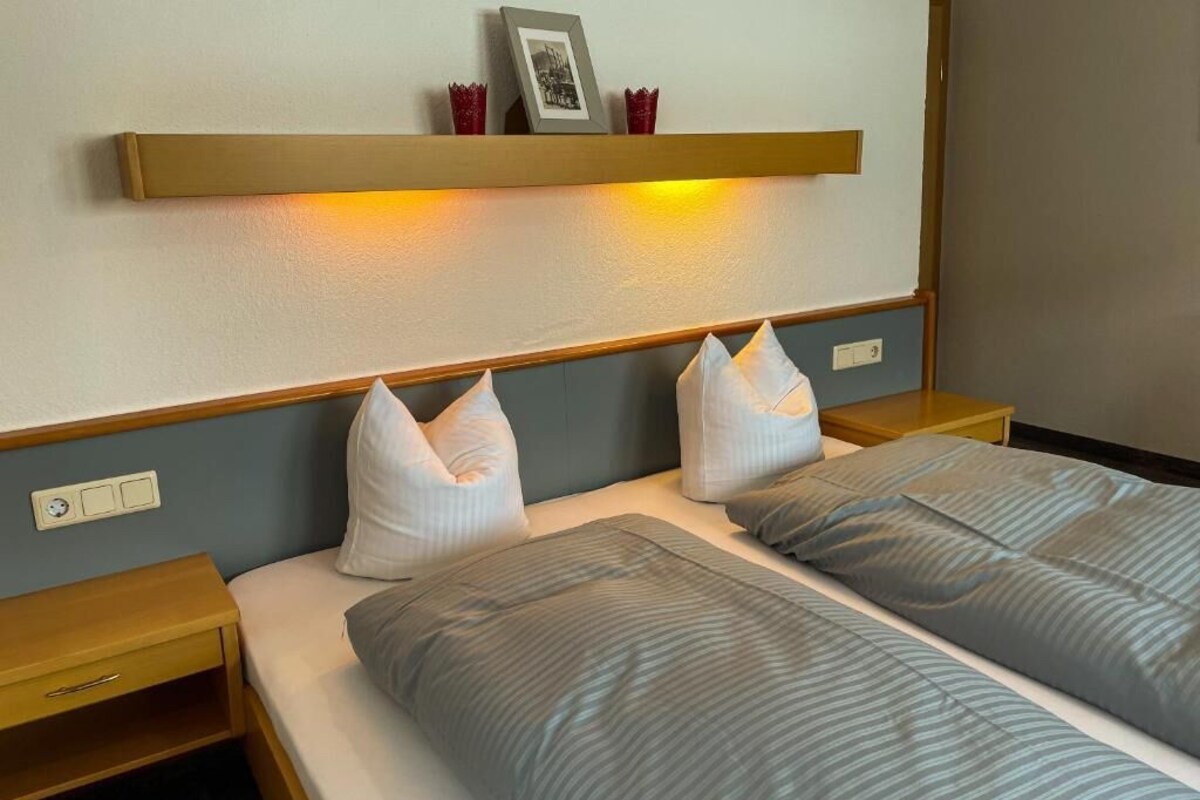 A hotel room with two beds, a bedside table, a nightstand, and a shelf above the beds.