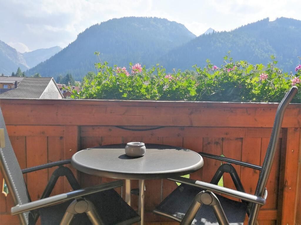 A round table with a chair, a small pot, and a wooden fence with flowers.